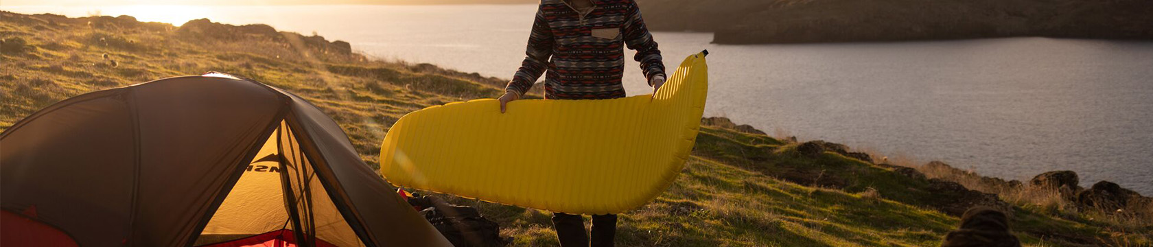Man legt zijn slaapmatje in een tent terwijl de zon ondergaat